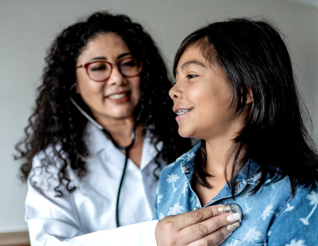 Smiling female healthcare clinician placing stethoscope on the chest of a young girl